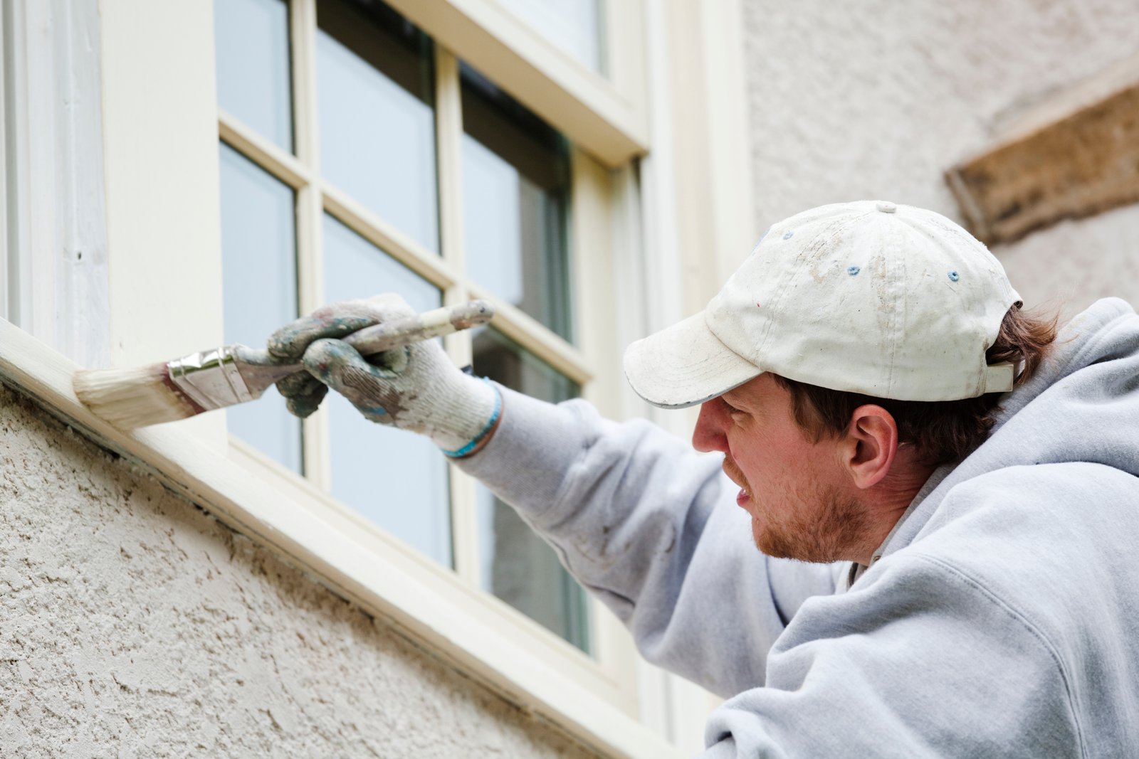 Subject: A house painter handyman painting the window trim of a residential home exterior.